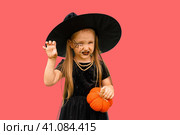 Portrait of winsome little witch smiling girl wearing a wizard hat and dressed in stylish carnival dress, looking at camera posing against pink background, Halloween. Стоковое фото, фотограф Ирина Старикова / Фотобанк Лори