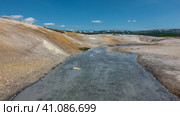 A stream from hot springs flows along a rocky bed. Yellow sulphurous deposits are visible on the soil. A mountain range against a blue sky. Kamchatka. The caldera of the extinct volcano Uzon. Стоковое фото, фотограф Вера Ивановна Кубарева / Фотобанк Лори