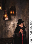 Vampire in cloak, top hat posing near chest in underground castle room, grinning at camera. Cover girl child actress in Dracula image smirking indoors. Theatre performing concept. Copy ad text space. Стоковое фото, фотограф Aleksandr Golubev / Фотобанк Лори