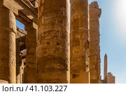 The colonnade of the hypostyle hall of the Karnak Temple. A row of columns against the blue sky. Hieroglyphs and carvings are visible. An obelisk in the distance. Egypt. Luxor (2021 год). Стоковое фото, фотограф Вера Ивановна Кубарева / Фотобанк Лори