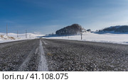 The highway goes forward and into the distance. White marking lines on the asphalt. There are electric poles on the roadsides in the snow. Bare trees on a hill. Blue sky. Altai. Chuysky tract. Стоковое фото, фотограф Вера Ивановна Кубарева / Фотобанк Лори