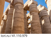 Colonnade in the hypostyle hall of the Karnak Temple of Luxor. Rows of tall ancient columns against the blue sky. Hieroglyphs and carvings are visible. Egypt (2021 год). Стоковое фото, фотограф Вера Ивановна Кубарева / Фотобанк Лори