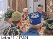Local residents of Siberian village celebrate Muslim holiday Kurban Bayram at their home table. Mullah saying prayer. Eid al-Adha (2021 год). Редакционное фото, фотограф Ирина Кононова / Фотобанк Лори