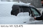 Person brushing fresh snow from car windows after snow storm blizzard. Morning routine difficulties of car owners in cold winter weather. Car window cleaning. Winter season. White snow. Vehicle care. Стоковое видео, видеограф Марина Демидюк / Фотобанк Лори
