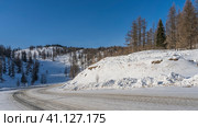 The highway curves around a snow-covered hill. Tire tracks are visible. Coniferous trees in snowdrifts on the side of the road. A mountain against a blue sky. Altai. Chuysky tract. Стоковое фото, фотограф Вера Ивановна Кубарева / Фотобанк Лори