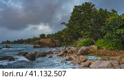 Picturesque boulders are scattered in the surf near the ocean shore. Turquoise waves beat against the rocks and foam. Lush tropical vegetation against the sky and clouds. Seychelles. Mahe. Стоковое фото, фотограф Вера Ивановна Кубарева / Фотобанк Лори
