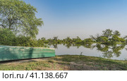 On the shore of the lake lies an old scratched upturned boat. Green trees are mirrored in the calm water. Blue sky. Copy space. India. Keoladeo Bird Sanctuary. Bharatpur. Стоковое фото, фотограф Вера Ивановна Кубарева / Фотобанк Лори