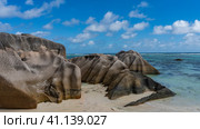 Picturesque whimsical boulders with wavy smoothed slopes lie on a sandy beach. The turquoise ocean is calm. Blue sky with clouds. Seychelles. La Digue. Anse Source D’Argent beach. Стоковое фото, фотограф Вера Ивановна Кубарева / Фотобанк Лори