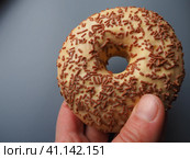 A doughnut or donut. A type of leavened fried dough. Sweet snack that can be homemade or purchased in bakeries, supermarkets, food stalls. Delicious pie with light icing on a gray background in hand. Стоковое фото, фотограф Юлия Петровская / Фотобанк Лори