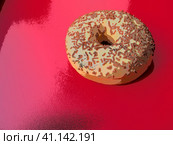 A doughnut or donut. A type of leavened fried dough. Sweet snack that can be homemade or purchased in bakeries, supermarkets, food stalls. Delicious pie with light icing on a red background, illusion. Стоковая иллюстрация, иллюстратор Юлия Петровская / Фотобанк Лори