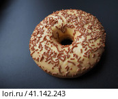 A doughnut or donut. A type of leavened fried dough. Sweet snack that can be homemade or purchased in bakeries, supermarkets, food stalls. Delicious pie with light icing on black or gray background. Стоковое фото, фотограф Юлия Петровская / Фотобанк Лори