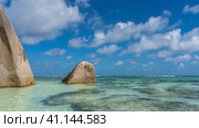 Picturesque granite cliffs rise above the calm turquoise ocean. Steep smoothed slopes. Blue sky with clouds. Seychelles. Anse Source D’Argent beach. La Digue. (2022 год). Стоковое фото, фотограф Вера Ивановна Кубарева / Фотобанк Лори