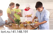 Interested enthusiastic teenager participating in culinary class of children group, engrossed in cooking process mirroring professional chef instructor steps. Стоковое видео, видеограф Яков Филимонов / Фотобанк Лори