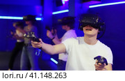 Cheerful emotional teenager in VR headset fully immersed in game, actively engaged in virtual reality world, manipulating objects or shooting targets with joysticks in hands. Стоковое видео, видеограф Яков Филимонов / Фотобанк Лори