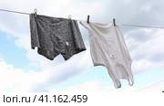 Leaky underpants and a T-shirt hang on a clothesline against a sky of clouds, a concept on the subject of poverty. Стоковое видео, видеограф Сергей Чайко / Фотобанк Лори