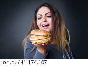 Happy beautiful young plus size model posing with hamburger on a gray studio background, xxl woman eating burger. Стоковое фото, фотограф Станислав Тарко / Фотобанк Лори