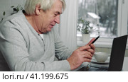 Serious senior man wearing glasses Talking mobile phone sitting at desk at home workplace with laptop. Retired male working chatting colleagues. Old worker talk on cellphone work on computer gadget. Стоковое видео, видеограф Марина Демидюк / Фотобанк Лори