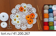 Summer needlework, hobby and craft. Box with set of multi-colored cotton yarn, hooks and flowers of daisies and marigolds on white handmade lace napkin. DIY concept. Top view, video, flat lay, closeup. Стоковое видео, видеограф Виктория Катьянова / Фотобанк Лори