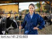 Smiling woman farmer with pitchfork in cowshed. Стоковое фото, фотограф Яков Филимонов / Фотобанк Лори