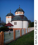Church behind the fence against the blue sky. Metallic black roof. The temple is renovated, freshly painted in white and ornamental colors. Wooden crosses are attached to the fence. Стоковое фото, фотограф Юлия Петровская / Фотобанк Лори