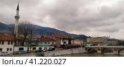 Sarajevo, Bosnia and Herzegovina - March 8, 2020: Sheher bridge over the Milatsk river. Spring. Turbid water in the river and bare trees. Turkish architecture and mosque. Mountains on the horizon. Редакционное фото, фотограф Юлия Петровская / Фотобанк Лори