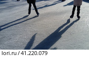 Children ride in a city park on an ice rink. Feet skater while skating on ice. The low winter sun weakly illuminates the ice. Dark shapes and long shadows on the surface. Sports movements. Стоковое фото, фотограф Юлия Петровская / Фотобанк Лори
