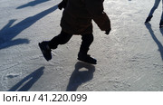 Children ride in a city park on an ice rink. Feet skater while skating on ice. The low winter sun weakly illuminates the ice. Dark shapes and long shadows on the surface. Sports movements. Стоковое фото, фотограф Юлия Петровская / Фотобанк Лори