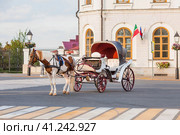 Travel around Russia. A carriage at the walls of the white Kremlin in Kazan, drawn by a horse in a skullcap. Russia, Republic of Tatarstan, Kazan, September 2023. Стоковое фото, фотограф Photojuli / Фотобанк Лори