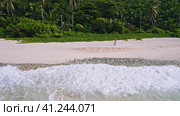 Aerial footage of young tanned woman running on the paradise beach with ocean waves rolling the shor. Стоковое фото, фотограф Igor Tichonow / Фотобанк Лори