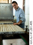 Farmer man working with automatic filling and seeding line for growing containerized seedlings of decorative plants in greenhouse. Стоковое фото, фотограф Яков Филимонов / Фотобанк Лори
