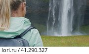 Closeup of female traveler back with backpack loking to Beautiful Seljalandsfoss waterfall Iceland. Стоковое видео, видеограф Igor Tichonow / Фотобанк Лори