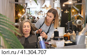 Portrait of young woman professional hair stylist talking to elderly female client in salon, choosing new hairdo. Стоковое видео, видеограф Яков Филимонов / Фотобанк Лори