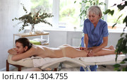 Focused professional mature masseuse performing anti-cellulite thigh massage to young female client in spa center. Стоковое видео, видеограф Яков Филимонов / Фотобанк Лори