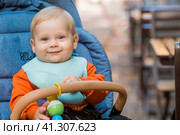 Portrait of a little boy 9 months old in the open air. A happy child in an autumn park is sitting in a stroller. Happy childhood and motherhood. Стоковое фото, фотограф Photojuli / Фотобанк Лори