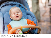 Portrait of a little boy 9 months old in the open air. A happy child in an autumn park is sitting in a stroller. Happy childhood and motherhood. Стоковое фото, фотограф Photojuli / Фотобанк Лори