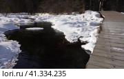 The stream winds between the snow-covered banks. Openwork frost at the water's edge. Dry grass is waving. A wooden footpath is laid on top. Bare trees in the distance. Altai. Стоковое видео, видеограф Вера Ивановна Кубарева / Фотобанк Лори