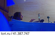 The young man cannot leave his laptop even lying in the bathtub, he has to wash without undressing. The interior of a hotel room is visible, the lights are dimmed, and water is splashing in the bathtub. Middle ground. Стоковое видео, видеограф Даниил Хабаров / Фотобанк Лори