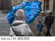 Женщина идет под зонтом во время дождя и во время сильного ветра по Манежной площади в центре города Москвы, Россия (2023 год). Редакционное фото, фотограф Николай Винокуров / Фотобанк Лори