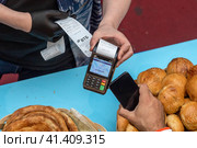 Мужчина прикладывает моблильный телефон к банковскому терминалу оплаты в кафе в городе Москве, Россия (2023 год). Редакционное фото, фотограф Николай Винокуров / Фотобанк Лори