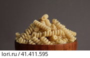 Gluten Free Cornmeal Pasta in wooden Bowl. Spiral Raw Macaroni from Blend of Corn and Rice flour rotating on Turntable. Close Up, Front View. Uncooked Rotini Pasta is Spinning. Food Background. Ad. Стоковое видео, видеограф Марина Демидюк / Фотобанк Лори