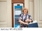 An elderly woman with shopping blonde is on the background in shopping center ATM. Стоковое фото, фотограф Андрей Аркуша / Фотобанк Лори