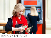 Mature blonde woman counting money near ATM. Стоковое фото, фотограф Андрей Аркуша / Фотобанк Лори