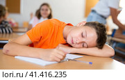 Bored tween schoolboy sleeping at desk in classroom during lesson. Стоковое фото, фотограф Яков Филимонов / Фотобанк Лори