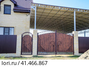 Brick house with a fence and gates. A large awning with a steel frame. View of a new built-up fence and a house made of bricks and corrugated metal. Стоковое фото, фотограф Леонид Еремейчук / Фотобанк Лори