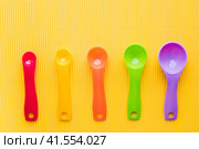 Мерные ложки на желтом фоне. Разноцветные пластиковые мерные ложки. Measuring spoons on a yellow background. Multi-colored plastic measuring spoons. Стоковое фото, фотограф Ольга Митряева / Фотобанк Лори