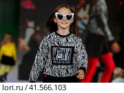 Девочка демонстрирует одежду из коллекции российского бренда Lucky child на подиуме фестиваля детской моды KIDS FASHION WEEK в "Центральном детском магазине на Лубянке" (ЦДМ) в Москве, Россия (2023 год). Редакционное фото, фотограф Николай Винокуров / Фотобанк Лори