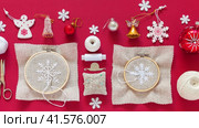 Video of handmade gifts for Christmas. Embroidery of snowflakes with white thread. Accessories for embroidery and Christmas tree toys nearby on red background. Preparing for Christmas holiday concept. Стоковое видео, видеограф Виктория Катьянова / Фотобанк Лори