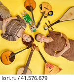 Women musicians in dresses with musical instruments on a yellow studio background. Happy artists with stringed musical instruments with smiles on faces. Стоковое фото, фотограф Андрей Журавлев / Фотобанк Лори
