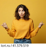 A young, pensive, insecure, rather attractive European girl of 20 years in a yellow casual blouse, spreads her hands questioningly, looking away. Created by AI. Стоковое AI-изображение, AI-художник Ярославский Максим / Фотобанк Лори