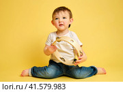 Toddler baby plays the tambourine, a child with a percussion musical instrument on a studio yellow background. Happy child musician playing hand drum. Kid aged one year four months. Стоковое фото, фотограф Андрей Журавлев / Фотобанк Лори